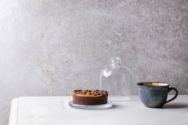 Sweet chocolate tartlet with cup of coffee espresso standing on white marble table with grey wall at background. Minimalist style. Copy space - Фото, изображение