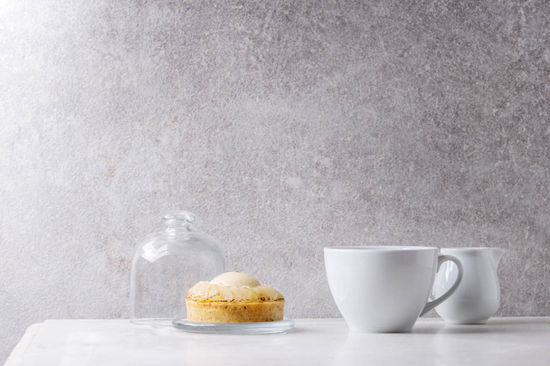 Sweet pear tartlet with cup of coffee espresso and jug of cream standing on white marble table with grey wall at background. Minimalist style. Copy space - Foto, afbeelding