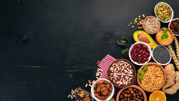 Various superfoods. Dried fruits, nuts, beans, fruits and vegetables. On a black wooden background. Top view. Free copy space. - Foto, afbeelding