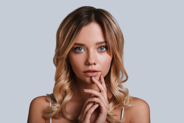 blonde young woman looking at camera while standing against grey background - Fotoğraf, Görsel