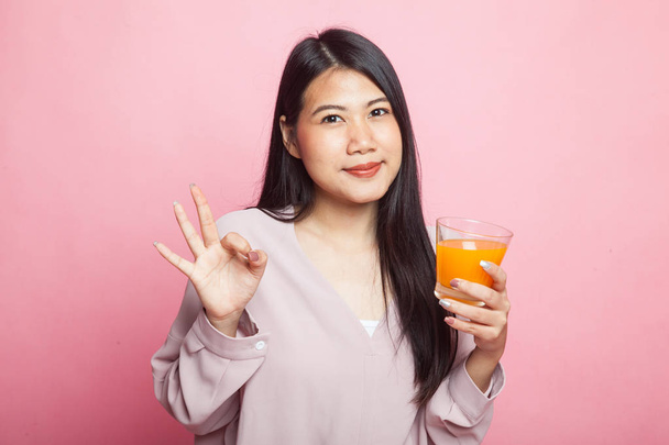 Young Asian woman drink orange juice show OK sign on pink background - Zdjęcie, obraz