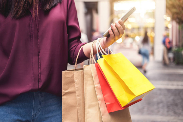 Consumerism, shopping, lifestyle concept, Young woman holding colorful shopping bags and smartphone enjoying in shopping. - Zdjęcie, obraz