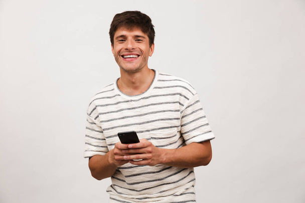 Image of happy cheerful handsome man standing isolated over white background wall using mobile phone. - Foto, Bild