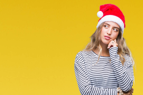 Mooie jonge blonde vrouw met kerst hoed op geïsoleerde achtergrond met hand op kin denken over de vraag, nadenkend expressie. Glimlachend met doordachte gezicht. Twijfel concept. - Foto, afbeelding