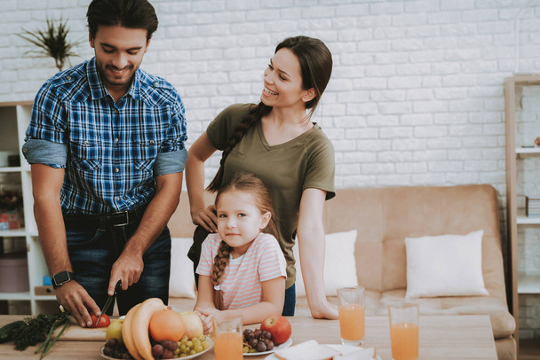 Father Prepares Breakfast. Family Breakfast. Family at Table. Fruit on Plate. Sandwich on Plate. White Plate. Juice in Glass. Happy family. Smiling People. Vegetables on Board. White Interior. - 写真・画像