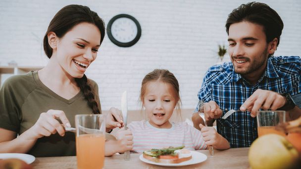 Family Breakfast. Parents Looking Sandwich. Breakfast for Happy Family. Fruit on Plate. Bread on Plate. White plate. Juice in Glass. Food on Table. Happy Family. Smiling People. Vegetarian Food. - Fotoğraf, Görsel