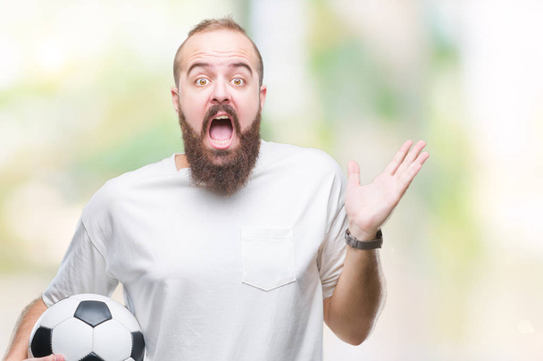 Jeune hipster caucasien tenant ballon de football sur fond isolé très heureux et excité, expression gagnante célébrant la victoire en criant avec un grand sourire et les mains levées
 - Photo, image