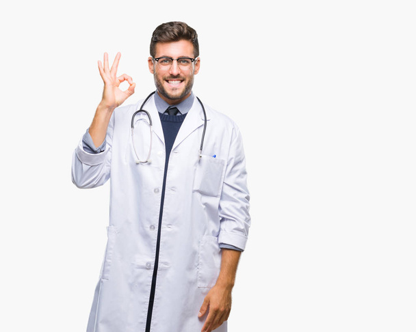 Fiatal jóképű orvos ember feletti elszigetelt háttér mosolyogva pozitív csinál a kéz és az ujjak ok jele. Sikeres kifejezés. - Fotó, kép