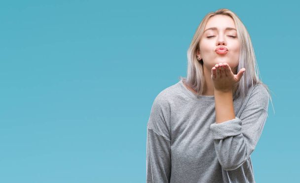 Young blonde woman over isolated background looking at the camera blowing a kiss with hand on air being lovely and sexy. Love expression. - Photo, Image