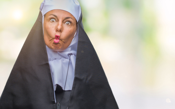 Middle age senior christian catholic nun woman over isolated background making fish face with lips, crazy and comical gesture. Funny expression. - Photo, Image