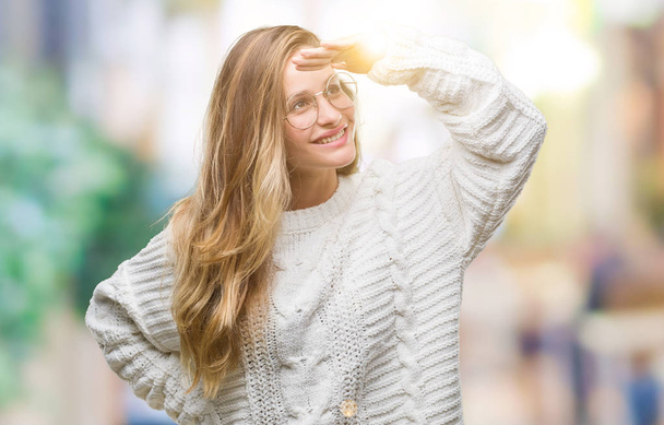 若い金髪美女着て冬セーターと分離背景非常に幸せと笑顔見ると遠くでサングラス頭の上の手します。概念を検索. - 写真・画像