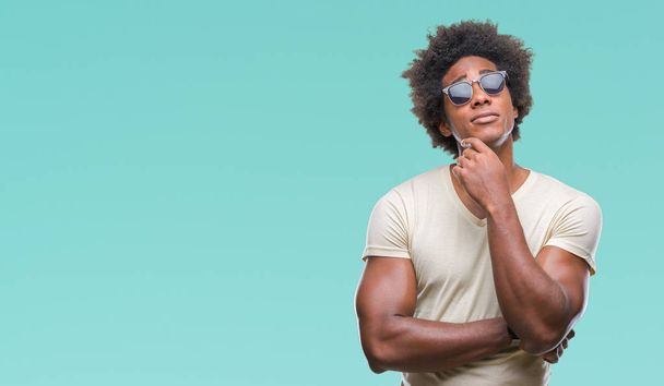 Afro american man wearing sunglasses over isolated background with hand on chin thinking about question, pensive expression. Smiling with thoughtful face. Doubt concept. - Фото, зображення