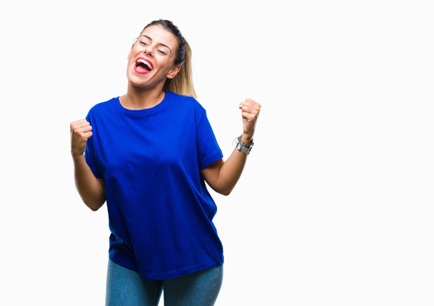 Young beautiful woman wearing casual blue t-shirt over isolated background very happy and excited doing winner gesture with arms raised, smiling and screaming for success. Celebration concept. - Photo, Image