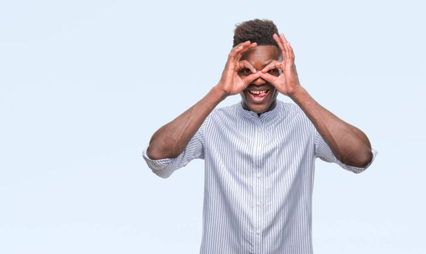 Jovem afro-americano sobre fundo isolado fazendo gesto ok como binóculos furando a língua para fora, olhos olhando através dos dedos. Expressão louca
. - Foto, Imagem