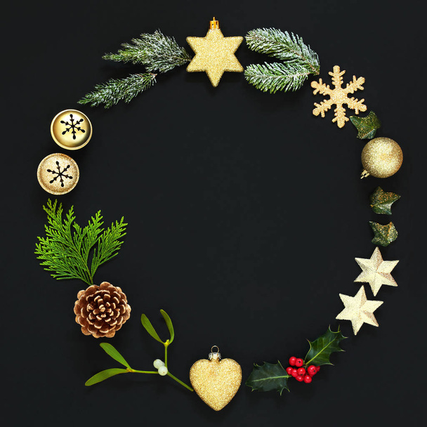 De kroon van Kerstmis garland met traditionele symbolen gouden bauble versieringen en winter flora op zwarte achtergrond - Foto, afbeelding