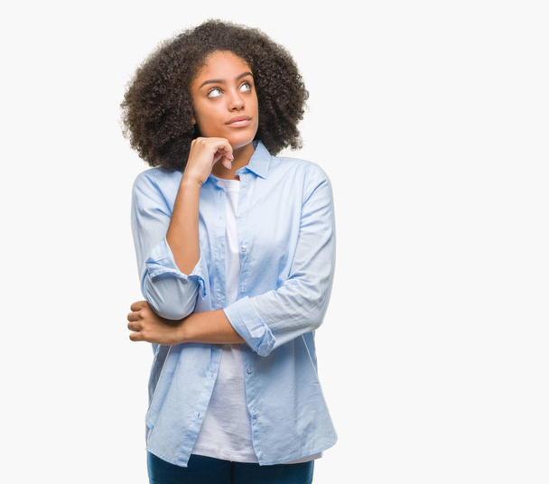Молодая афро-американка на изолированном фоне с рукой на подбородке думает о вопросе, задумчивом выражении лица. Улыбается с вдумчивым лицом. Концепция сомнений
. - Фото, изображение