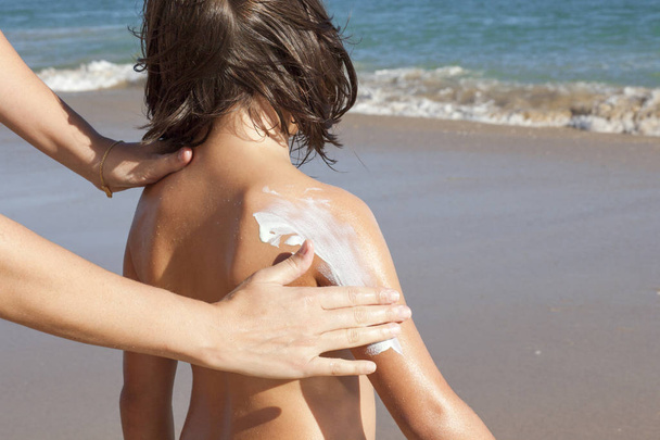 Anne kızını koluna güneş kremi krem uygulamak. Pastoral plaj arka plan  - Fotoğraf, Görsel