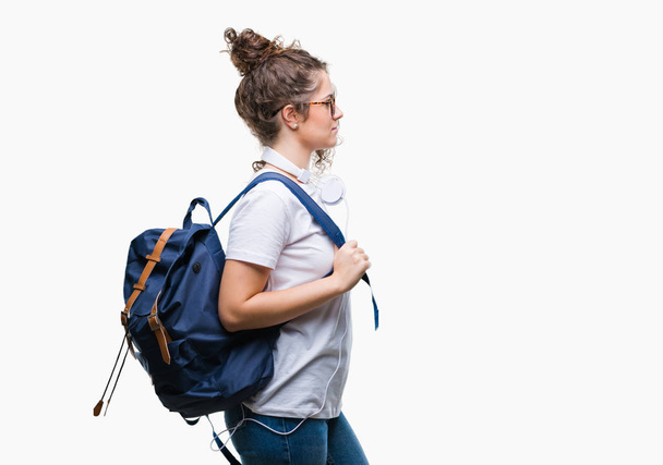 Молодая брюнетка студентка носит рюкзак и наушники на изолированном фоне глядя в сторону, расслабиться профиль позировать с естественным лицом с уверенной улыбкой
. - Фото, изображение
