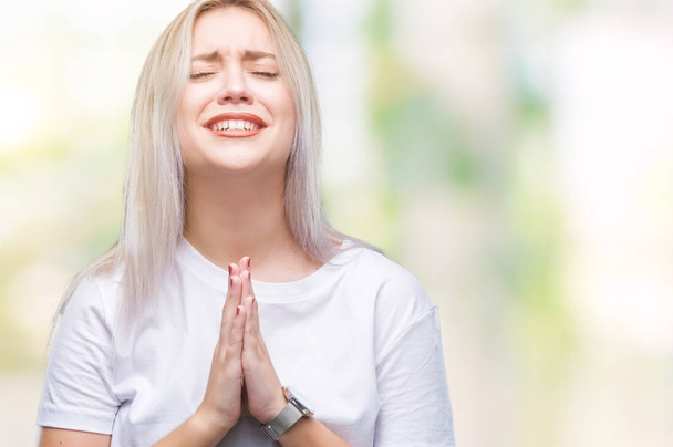 Jonge blonde vrouw op geïsoleerde achtergrond bedelen en bidden met handen samen met hoop uitdrukking op gezicht heel emotioneel en bang. Vragen om vergeving. Religie concept. - Foto, afbeelding