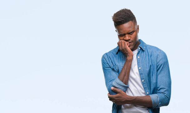 Jonge Afro-Amerikaanse man over geïsoleerde achtergrond op zoek gestresst en nerveus met handen op mond nagels te bijten. Angst probleem. - Foto, afbeelding