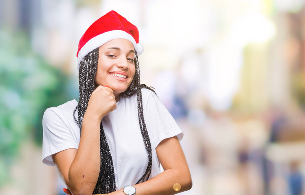Young braided hair african american girl wearing christmas hat over isolated background with hand on chin thinking about question, pensive expression. Smiling with thoughtful face. Doubt concept. - Foto, Imagen