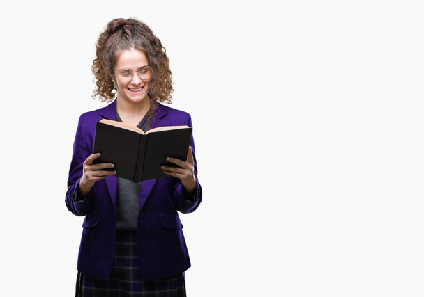 Jonge brunette student meisje dragen van school uniform lezen van een boek over geïsoleerde achtergrond met een blij gezicht permanent en lachend met een vertrouwen glimlach weergeven tanden - Foto, afbeelding