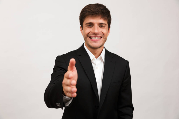Image of handsome cheerful young businessman standing isolated over white background wall give a hand to you for handshake. - Photo, image