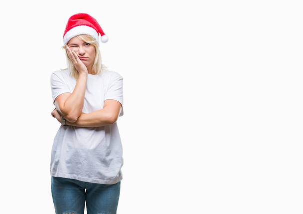 Νέοι όμορφη ξανθιά γυναίκα που φοράει καπέλο Χριστουγέννων πάνω από απομονωμένες υπόβαθρο σκέψης ψάχνει κουρασμένη και τρυπημένο με προβλήματα κατάθλιψης με σταυρωμένα χέρια. - Φωτογραφία, εικόνα