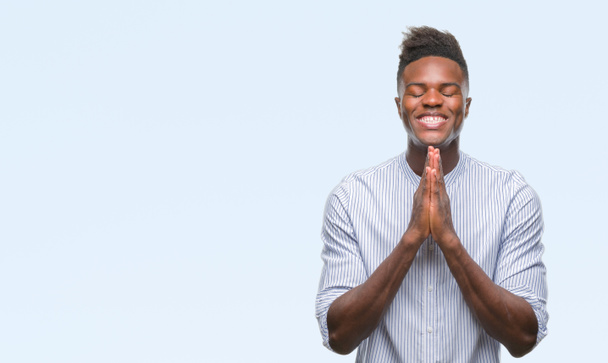 Jovem afro-americano sobre fundo isolado rezando com as mãos juntas pedindo perdão sorrindo confiante
. - Foto, Imagem