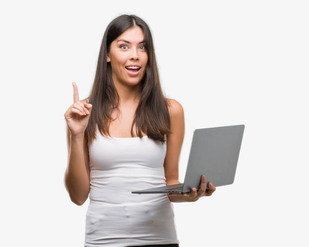 Young hispanic woman using computer laptop surprised with an idea or question pointing finger with happy face, number one - Foto, Imagem