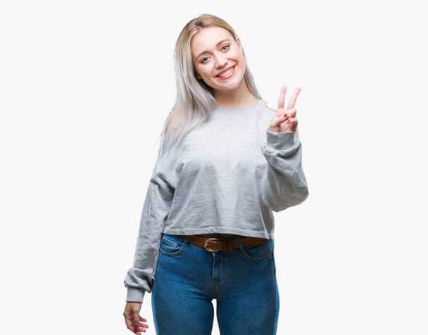 Young blonde woman over isolated background smiling with happy face winking at the camera doing victory sign. Number two. - Fotografie, Obrázek