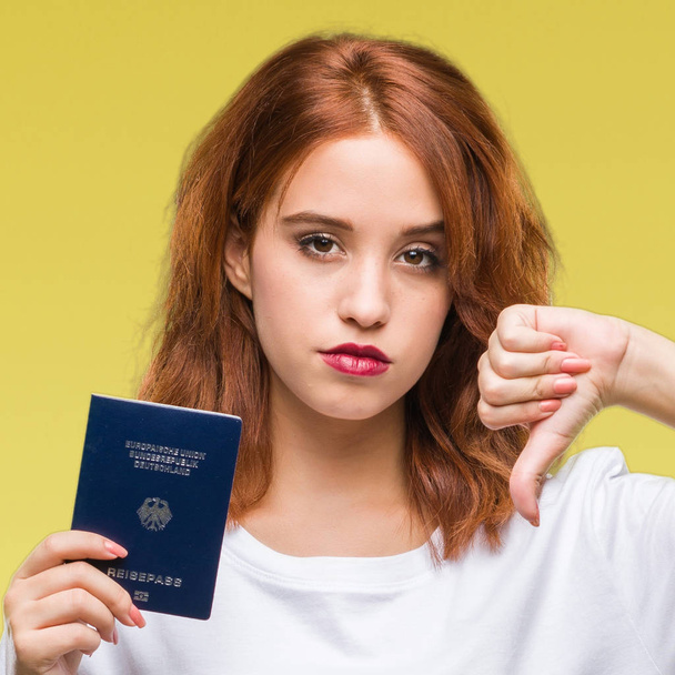 Fiatal gyönyörű nő útlevéllel Németország felett Haragos arc, negatív előjellel mutatja ellenszenv a hüvelykujját lefelé, elutasítás koncepció elszigetelt háttér - Fotó, kép
