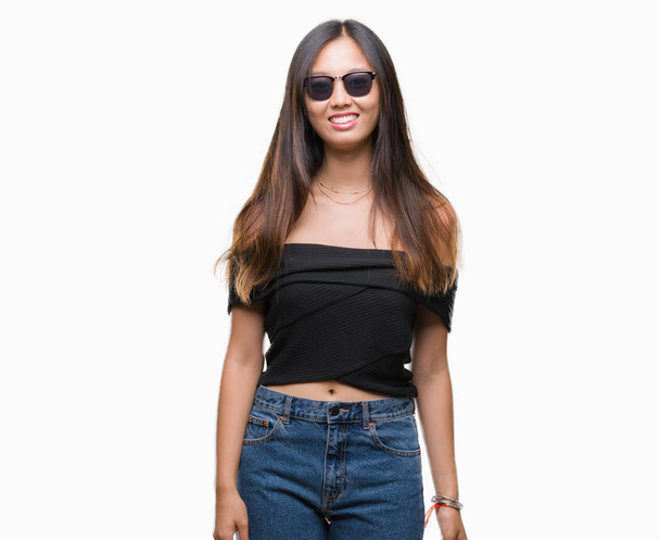 Young asian woman wearing sunglasses over isolated background with a happy and cool smile on face. Lucky person. - Foto, afbeelding