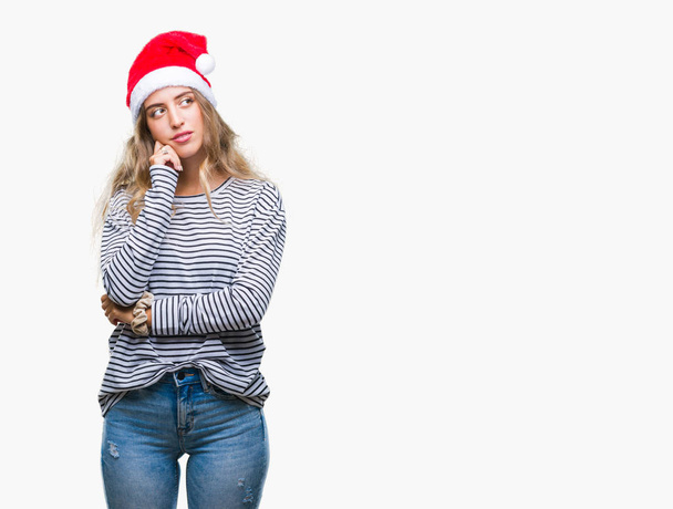 Beautiful young blonde woman wearing christmas hat over isolated background with hand on chin thinking about question, pensive expression. Smiling with thoughtful face. Doubt concept. - Photo, Image