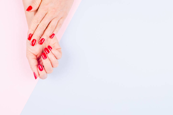 De handen van de vrouw met stijlvolle rode manicure op pastel blauwe en roze achtergrond. Vakantie-, partij- en schoonheidsbehandelingen concept. Horizontale - Foto, afbeelding