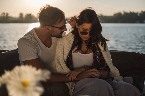 Coppia travagliata innamorata che si tiene per mano mentre siede vicino al fiume. Bellissimo tramonto autunnale
 - Foto, immagini