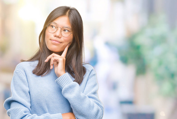 Młoda kobieta azjatyckich swetrze zima na na białym tle ręką na podbródek myślenia o pytanie, wyrażenie zamyślony. Uśmiech z twarzy przemyślane. Koncepcja wątpliwości. - Zdjęcie, obraz