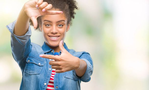 Jovem afro-americana sobre fundo isolado sorrindo fazendo moldura com mãos e dedos com rosto feliz. Conceito de criatividade e fotografia
. - Foto, Imagem