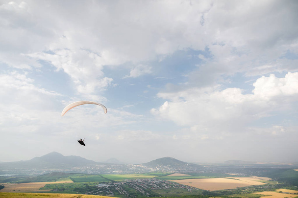 A white-orange paraglider flies over the mountainous terrain - Fotografie, Obrázek
