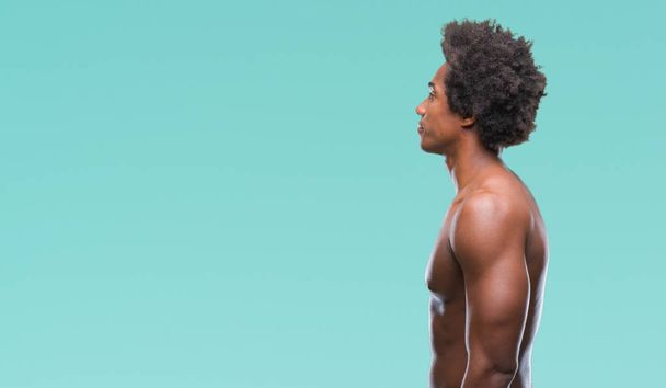 Afroamerikaner ohne Hemd Mann zeigt nackten Körper über isolierten Hintergrund Blick zur Seite, entspannen Profil Pose mit natürlichem Gesicht mit selbstbewusstem Lächeln. - Foto, Bild