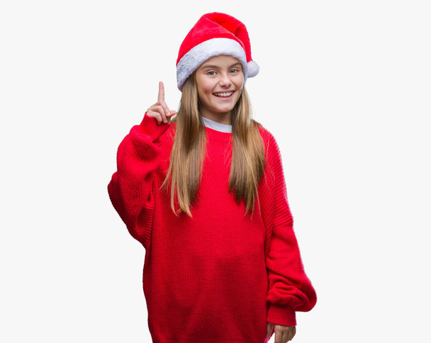 Young beautiful girl wearing christmas hat over isolated background showing and pointing up with finger number one while smiling confident and happy. - Photo, image