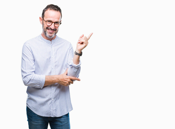 Middle age hoary senior man wearing glasses over isolated background with a big smile on face, pointing with hand and finger to the side looking at the camera. - Photo, image