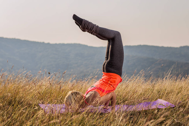 Beautiful woman doing yoga in the nature,Vrschikasana / Scorpion pose.Image is intentionally toned. - Photo, image