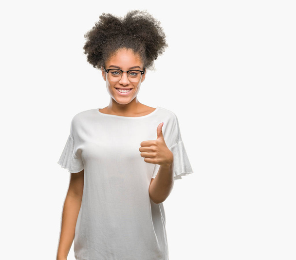 Young afro american woman wearing glasses over isolated background doing happy thumbs up gesture with hand. Approving expression looking at the camera with showing success. - Photo, image