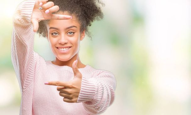 笑顔の幸せそうな顔で指と手作りフレーム分離の背景に冬のセーターを着ている若いアフロ ・ アメリカ人女性。創造性と写真のコンセプト. - 写真・画像