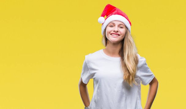 若い美しい金髪女性の顔に幸せとクールな笑みを浮かべて隔離された背景にクリスマス帽子をかぶっています。幸運な人. - 写真・画像