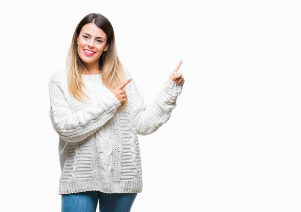 Молодая красивая женщина случайный белый свитер на изолированном фоне улыбаясь и глядя на камеру указывая двумя руками и пальцами в сторону
. - Фото, изображение