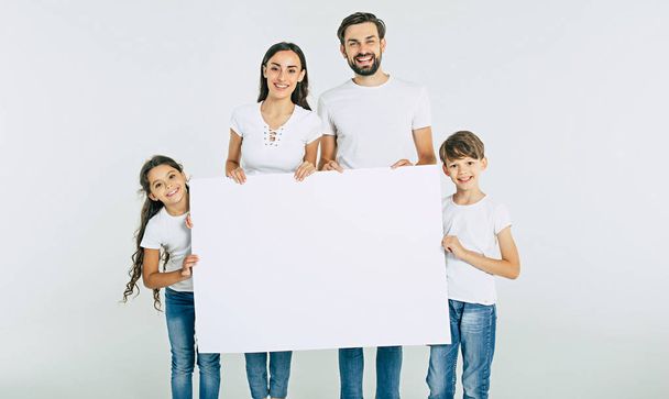 Young happy family holding white sheet of blank paper on white background  - Foto, immagini