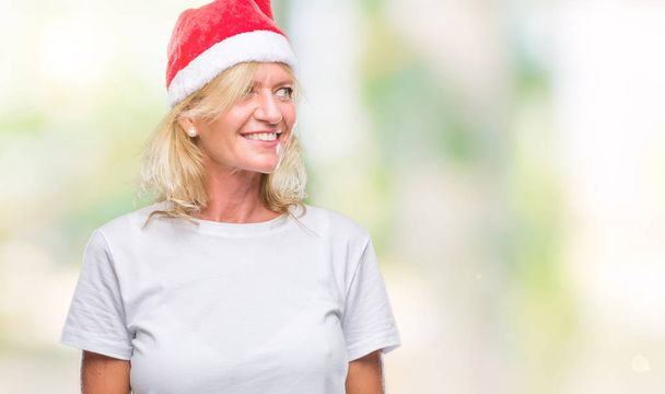 中年の金髪女性上クリスマスの帽子をかぶって分離背景が笑顔で側に自然な表現の顔に離れています。自信を持って笑ってください。. - 写真・画像