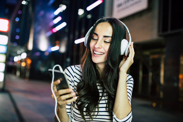 Young smiling woman listening to music in headphones with smartphone  - Fotoğraf, Görsel